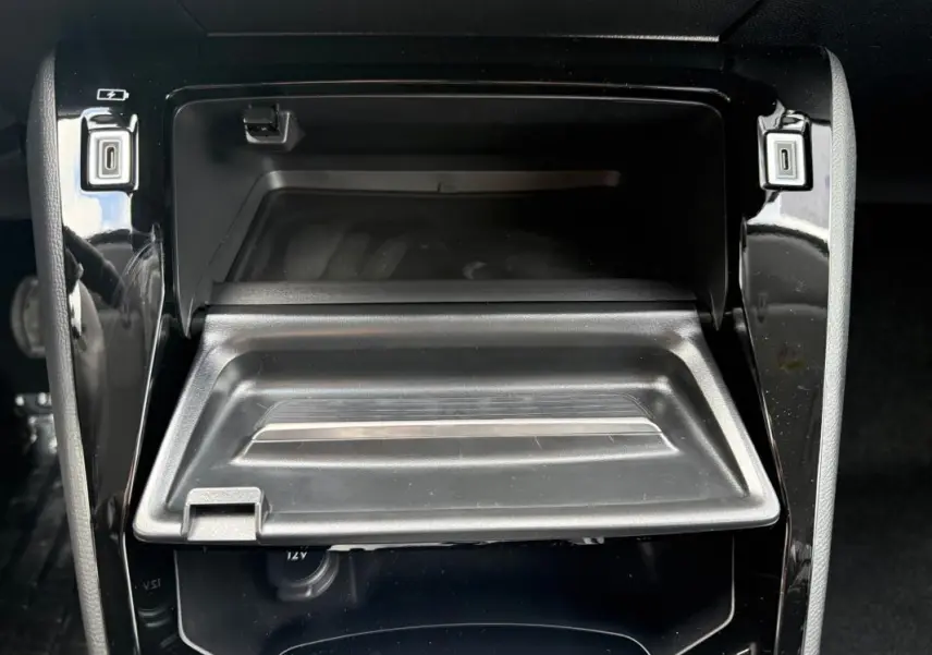 Vue rapprochée du rangement central ouvert de la Peugeot 208 Hybrid 145 gris, avec prise 12V visible en dessous.