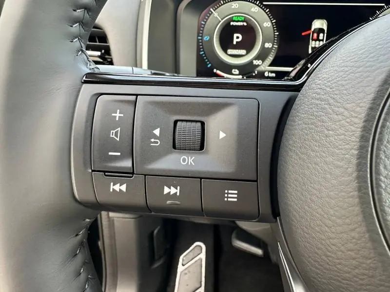 Gros plan sur les commandes au volant à gauche du Nissan Qashqai Hybrid e-POWER 2025, avec tableau de bord numérique en arrière-plan.