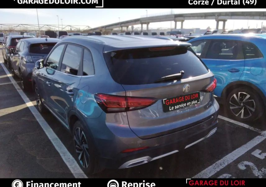 Vue 3/4 arrière droite d'un MG Motor ZS gris clair garé, avec feux arrière LED et toit ouvrant visible.