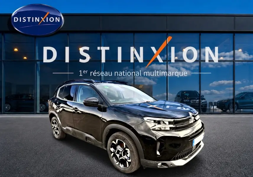 SUV Citroën C5 Aircross noir vu en 3/4 avant droit, avec jantes alu et barres de toit visibles devant un showroom.