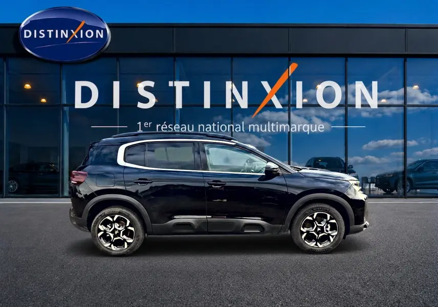 Profil droit d’un Citroën C5 Aircross noir 2025 avec jantes alu et barres de toit devant une vitrine Distinxion.