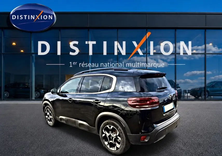 Vue 3/4 arrière droite d'un Citroën C5 Aircross noir brillant avec jantes alu et barres de toit visibles.