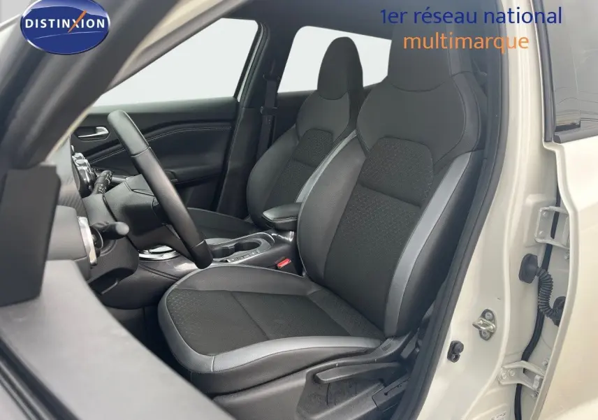 Vue intérieure côté conducteur du Nissan Juke blanc nacré, mettant en valeur les sièges noirs au design moderne et la console centrale.