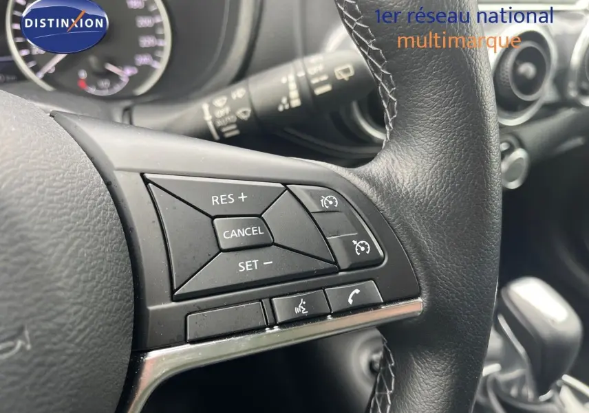 Gros plan sur les commandes de régulateur de vitesse au volant cuir noir du Nissan Juke blanc nacré 2024.