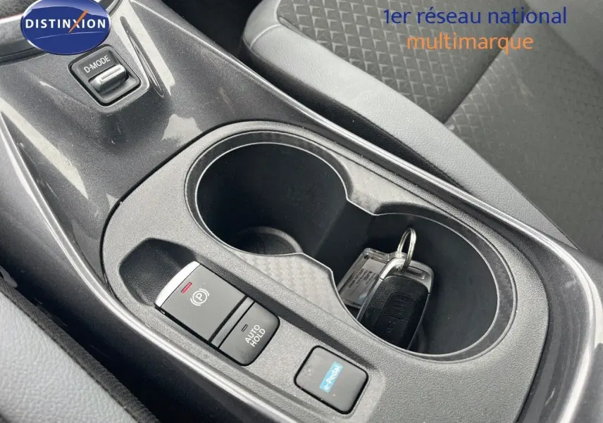 Gros plan sur la console centrale noire du Nissan Juke blanc nacré, avec porte-gobelets et clés posées.