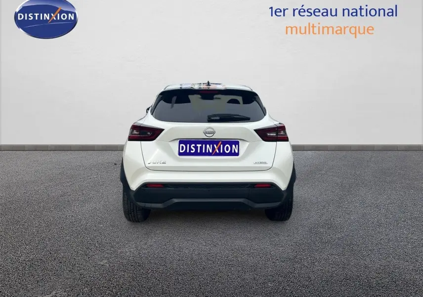 Vue arrière d'un Nissan Juke blanc nacré 2024 avec logo hybride et plaque Distinxion visible.