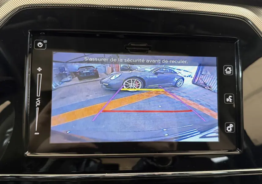 Écran tactile montrant la caméra de recul avec vue arrière d’un véhicule gris stationné en intérieur.