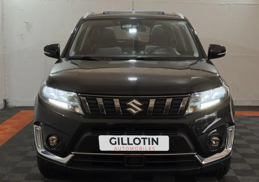 Suzuki Vitara noir vue de face, phares LED allumés et calandre chromée distinctive visible.