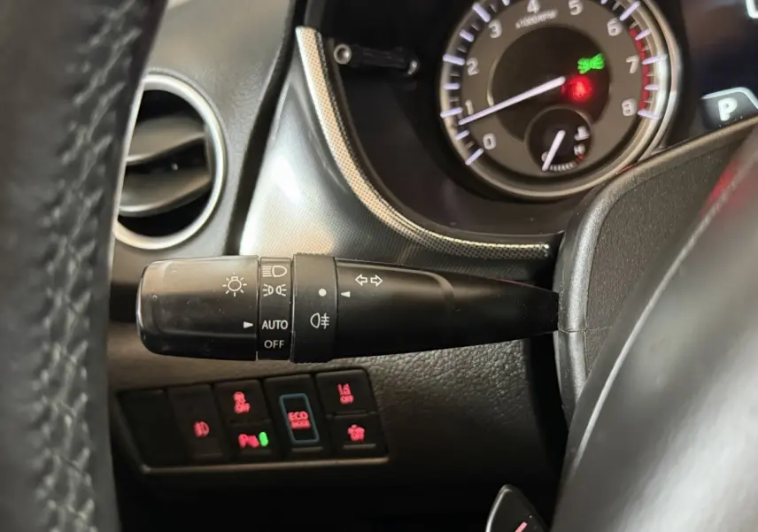 Gros plan sur la manette des phares et les boutons de contrôle du tableau de bord du Suzuki Vitara 1.5 Hybrid noir, intérieur.