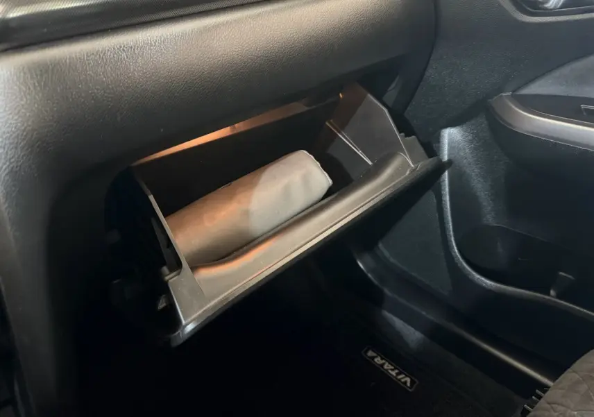 Gros plan sur la boîte à gants ouverte côté passager du Suzuki Vitara noir, avec un objet beige à l'intérieur.