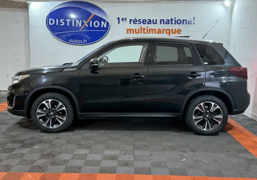 Profil côté gauche du Suzuki Vitara noir 2022 dans un showroom avec jantes alliage et vitres teintées.