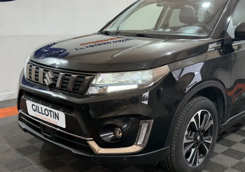 Vue 3/4 avant droit d'un Suzuki Vitara noir 2022 avec calandre chromée et phares LED allumés.