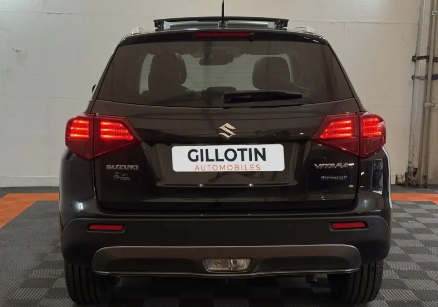 Vue arrière d'un Suzuki Vitara noir 2022 avec feux allumés et logo hybride visible sur le hayon.