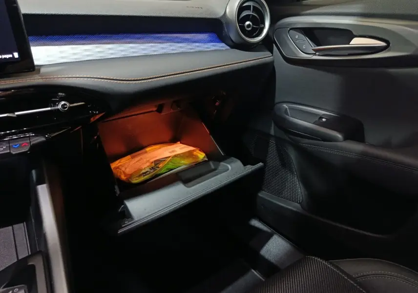 Intérieur de l'Alfa Romeo Tonale 2023, vue côté passager, boîte à gants ouverte avec éclairage orange.