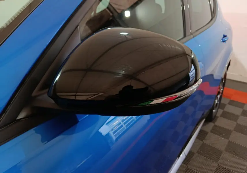 Gros plan sur le rétroviseur noir côté conducteur d'une Alfa Romeo Tonale bleu 2023 avec drapeau italien intégré.