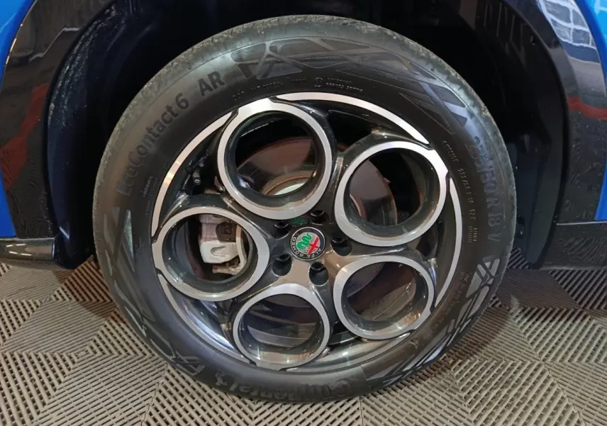 Gros plan sur la roue avant droite de l'Alfa Romeo Tonale bleu, avec jante distinctive à cinq cercles et logo central.