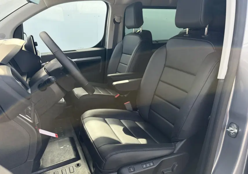 Vue intérieure côté conducteur du Citroën Jumpy gris acier, sièges cuir noirs avec accoudoirs et volant chauffant.