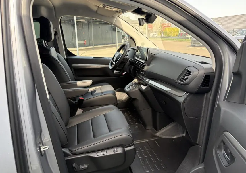 Vue intérieure côté conducteur du Citroën Jumpy gris acier, montrant sièges cuir noirs et tableau de bord moderne.