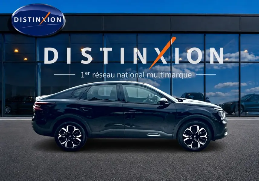 Profil côté gauche de la Citroën C4 X noire 2025 avec jantes alu et lignes fluides devant une vitrine Distinxion.