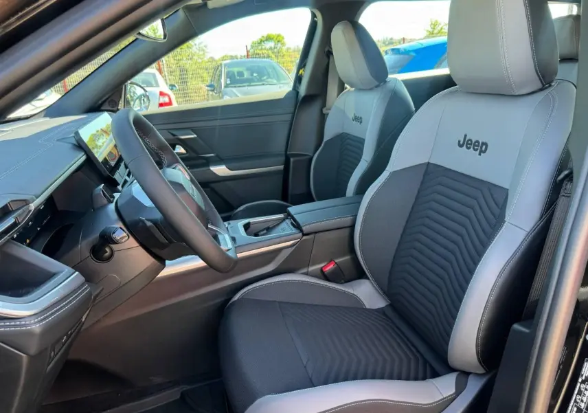 Vue intérieure côté conducteur du Jeep Compass 2026 avec sièges tissu gris/anthracite et logo Jeep brodé.