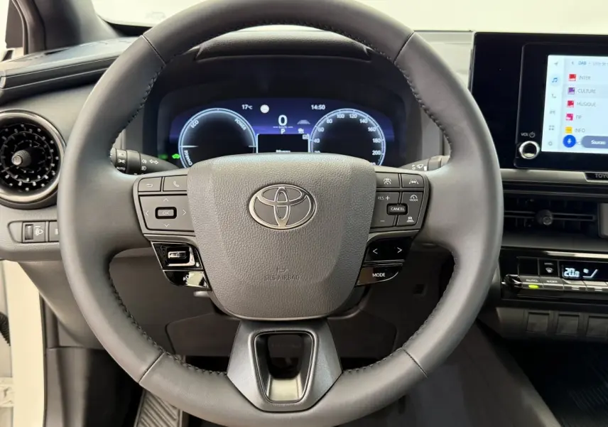 Vue rapprochée du volant cuir noir du Toyota C-HR 1.8 Hybride 2024 avec tableau de bord numérique et écran tactile.