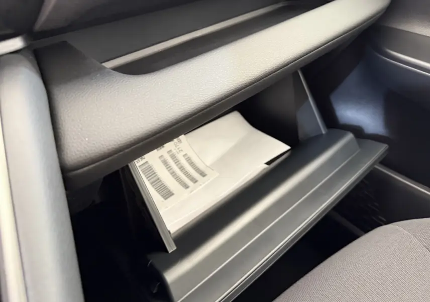 Gros plan sur la boîte à gants ouverte du Toyota C-HR 1.8 Hybride blanc, montrant des documents à l'intérieur.