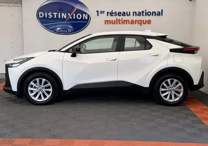 Profil côté gauche du Toyota C-HR 1.8 Hybride blanc 2024 avec jantes alliage et lignes anguleuses marquées.