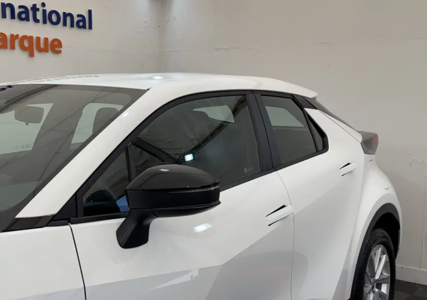 Vue côté gauche avant du Toyota C-HR 1.8 Hybride blanc avec rétroviseur noir et poignées affleurantes.