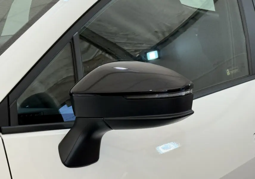 Rétroviseur côté gauche noir brillant du Toyota C-HR blanc 2024, avec clignotant intégré visible en gros plan.