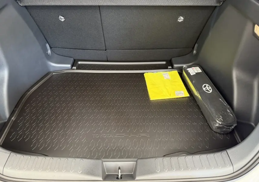 Coffre ouvert du Toyota C-HR blanc 2024, vue intérieure avec tapis noir et accessoires de sécurité visibles.