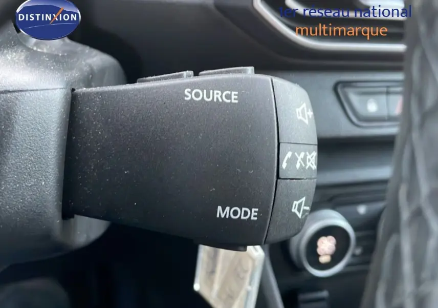 Gros plan sur la commande au volant du Dacia Jogger 2025, boutons source et mode visibles dans l'habitacle noir.