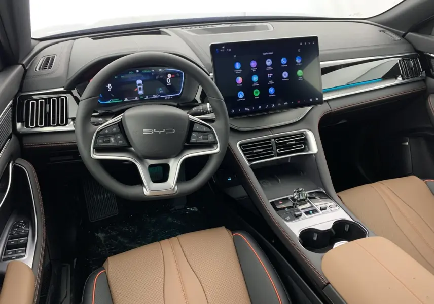 Vue intérieure avant du BYD SEAL U 2025 avec tableau de bord numérique, écran tactile 15,6'' et sièges en similicuir brun.