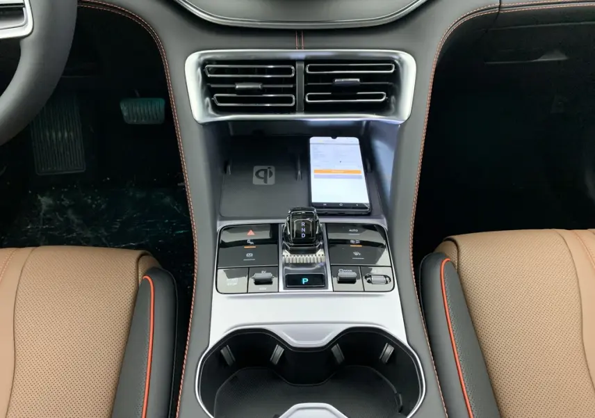 Vue plongeante sur la console centrale du BYD SEAL U 2025 Time Grey, avec levier de vitesses, chargeur sans fil et sièges marron à surpiqûres orange.