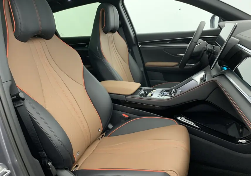 Vue intérieure côté conducteur du BYD SEAL U 2025, sièges en similicuir noir et marron avec surpiqûres orange et accoudoir central beige.