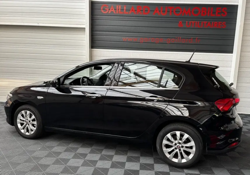 Profil gauche d'une FIAT TIPO noire de 2017, compacte avec jantes alliage et vitres teintées, en intérieur showroom.
