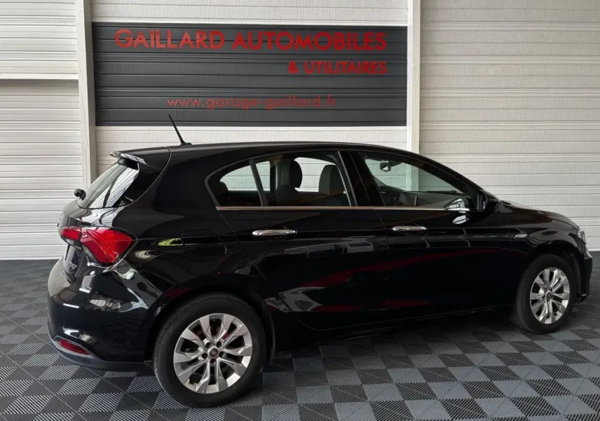 Vue latérale droite d'une FIAT Tipo noire 5 portes garée en intérieur avec jantes alliage et feux arrière visibles.