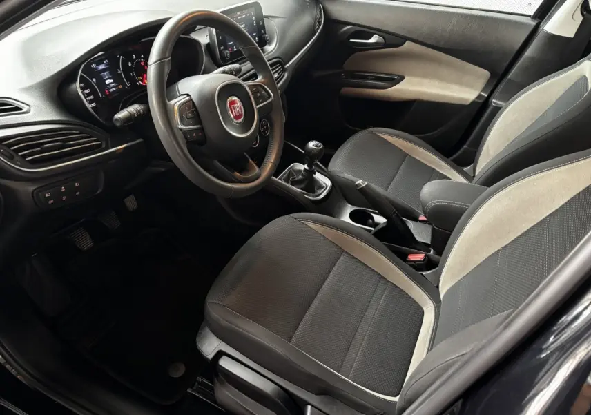Intérieur avant droit de la Fiat Tipo 2017, volant cuir alu multifonctions et sièges tissu noir avec surpiqûres grises.