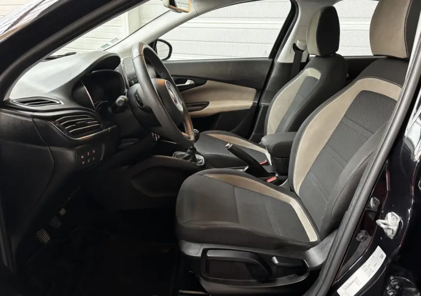 Vue intérieure côté conducteur de la Fiat Tipo noire, montrant les sièges bi-matière et le volant multifonctions cuir alu.