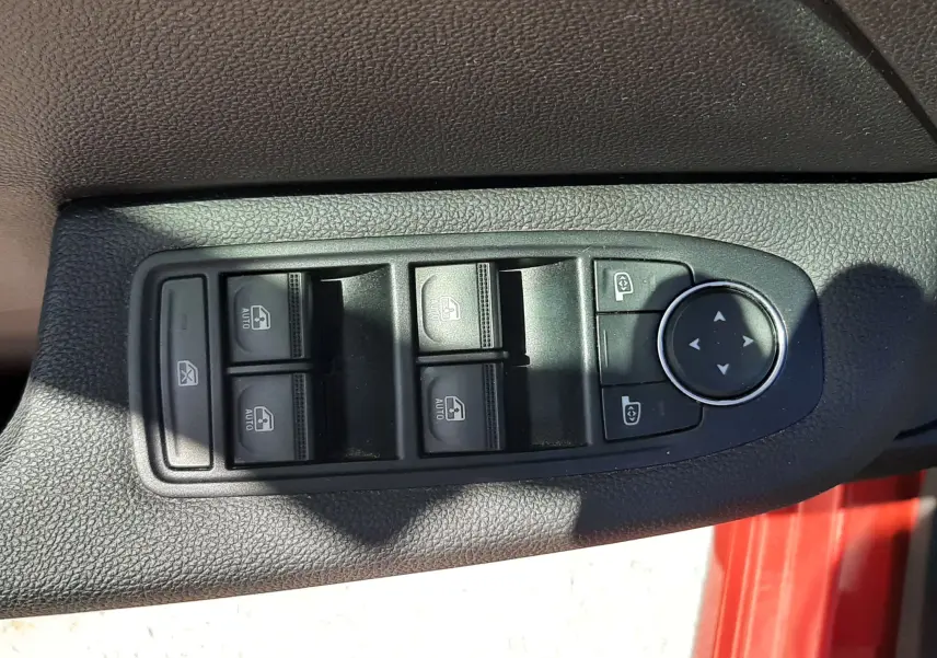 Gros plan sur les commandes des vitres électriques et rétroviseurs sur la porte côté conducteur d'une Renault Clio V rouge.