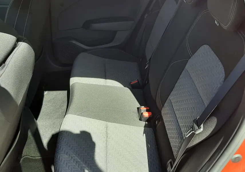 Vue intérieure côté arrière droit de la Renault Clio V rouge, montrant les sièges arrière en tissu gris noir avec ceinture de sécurité.