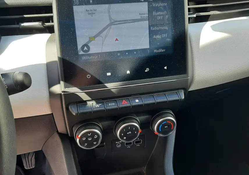 Vue rapprochée de la console centrale de la Renault Clio V rouge, avec écran tactile et commandes de climatisation.