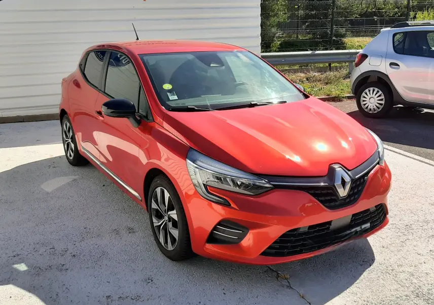 Renault Clio V rouge vue 3/4 avant droit, avec phares LED et jantes alliage bicolores, stationnée en extérieur.