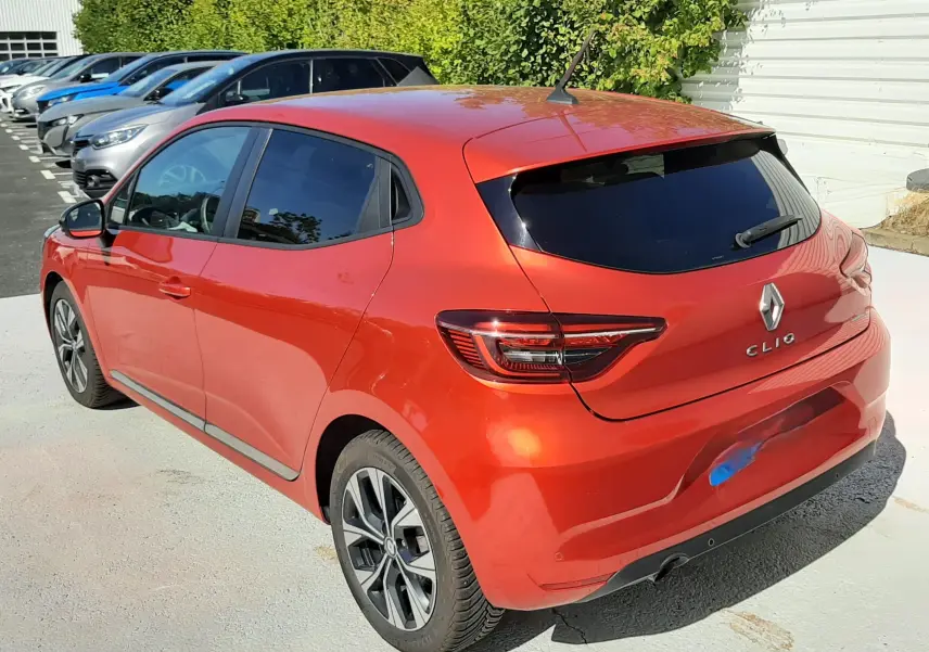 Vue 3/4 arrière droite d'une Renault Clio V rouge 5 portes, avec vitres teintées et jantes alliage bicolores.