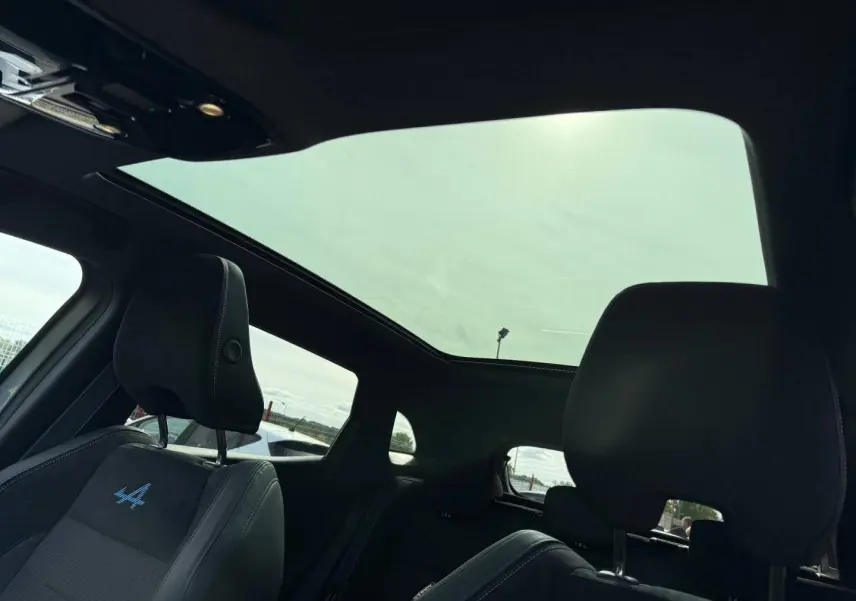 Vue intérieure du Renault Austral 2026, toit panoramique, sièges avant noirs avec logo Alpine bleu brodé.