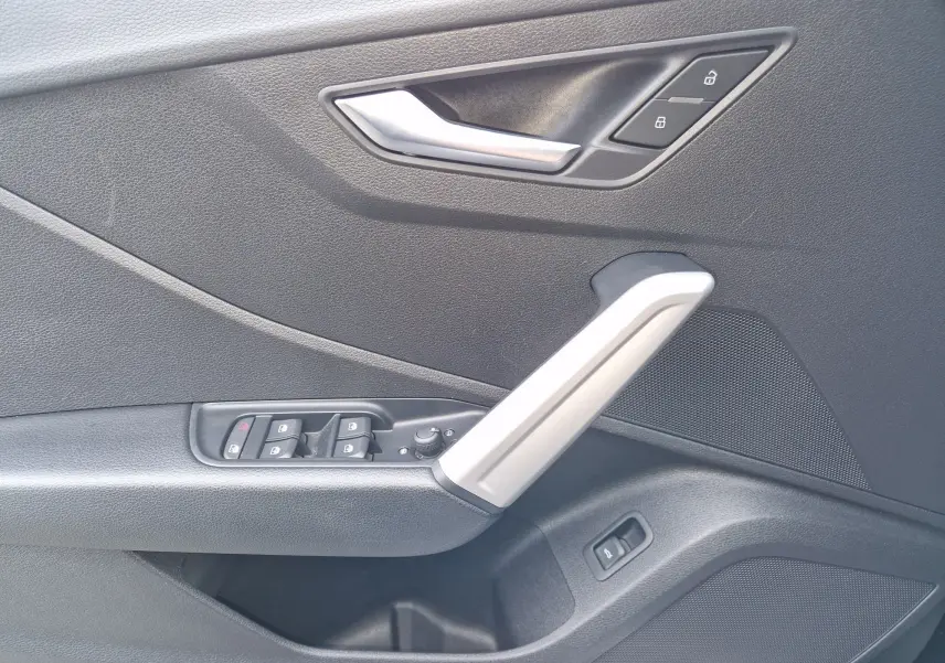 Détail de la porte côté gauche de l'Audi Q2 2023 noir mito metal avec commandes de vitres et poignée argentée.