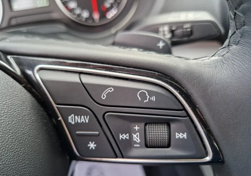 Gros plan sur les commandes vocales et audio noires du volant de l'Audi Q2 2023 finition Advanced.