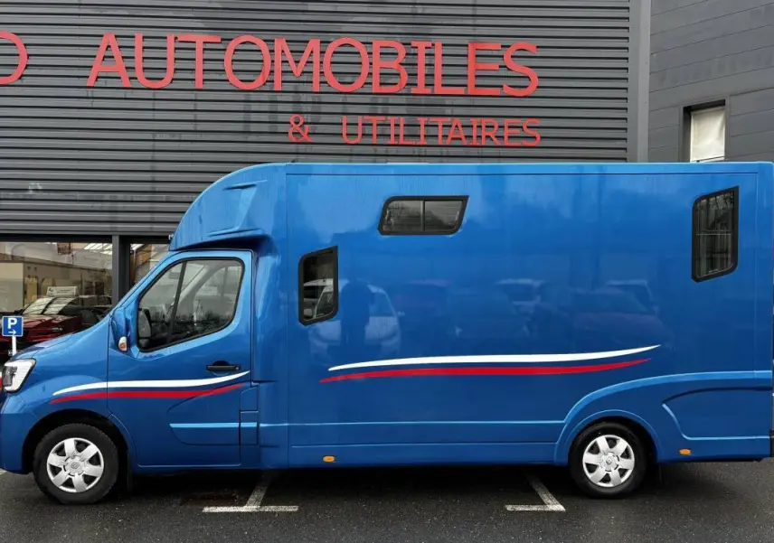 Vue de profil côté gauche d’un Renault Master bleu avec bandes blanches et rouges, vitres latérales et cabine surélevée.