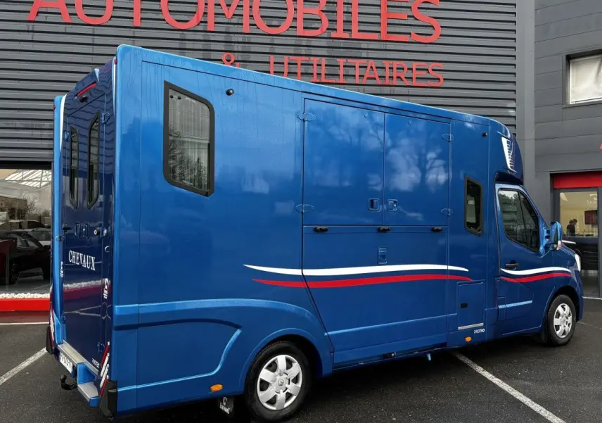 Vue 3/4 arrière droite d’un Renault Master bleu avec marquage tricolore et aménagement chevaux visible sur la porte arrière.
