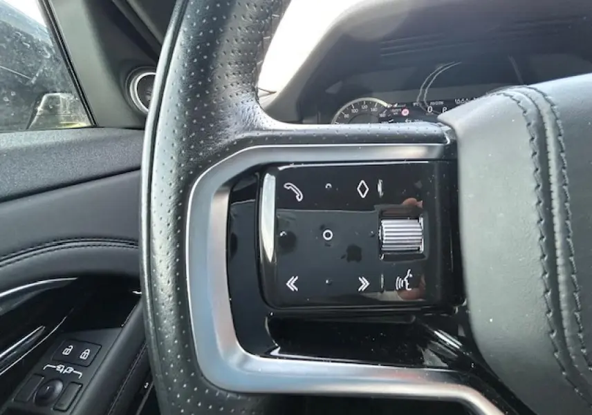 Gros plan sur le volant cuir perforé côté gauche du Range Rover Evoque gris foncé avec commandes intégrées et tableau de bord en arrière-plan.