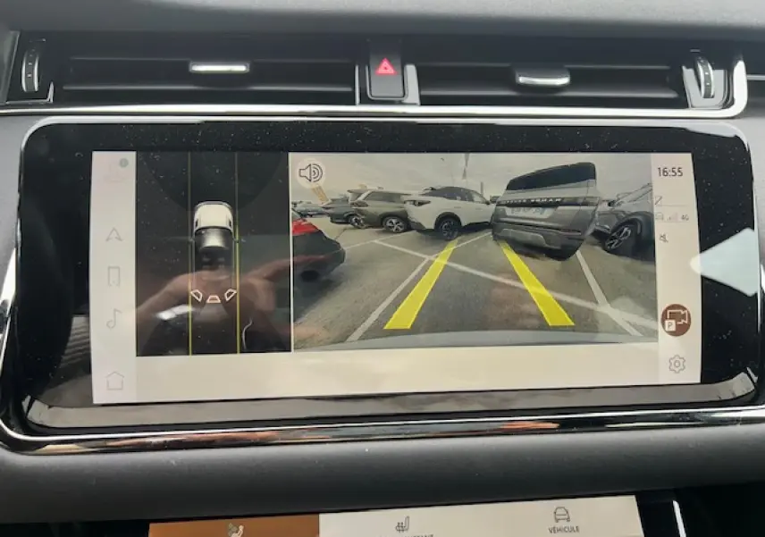 Écran tactile intérieur montrant la caméra de recul avec vue arrière sur un parking et plusieurs véhicules gris et blancs.
